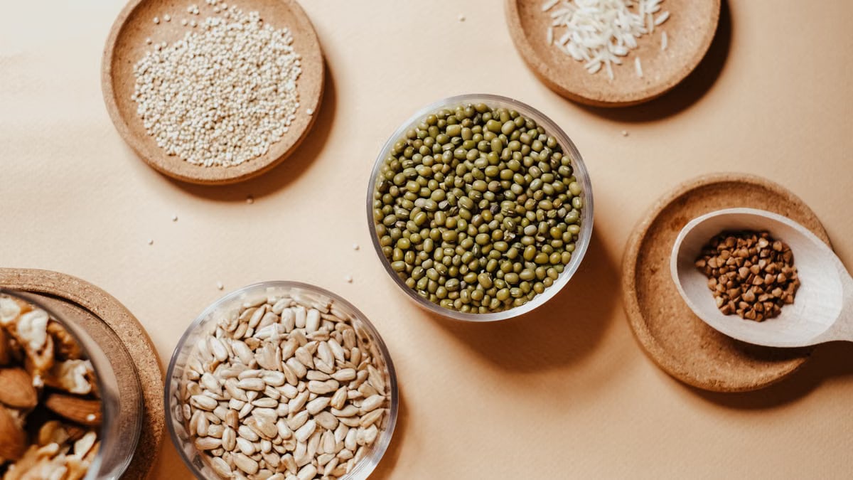 Flat lay of assorted seeds and nuts in rustic saucers on a neutral background, showcasing natural textures.